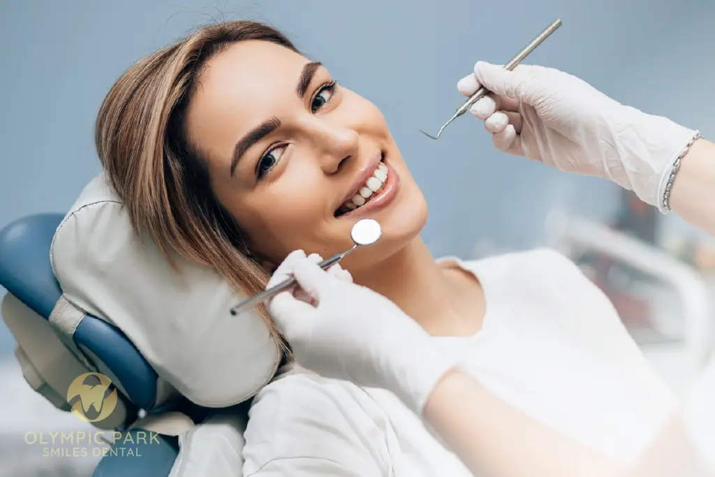 Smiling woman in a dental chair while a dentist holds a mirror and probe