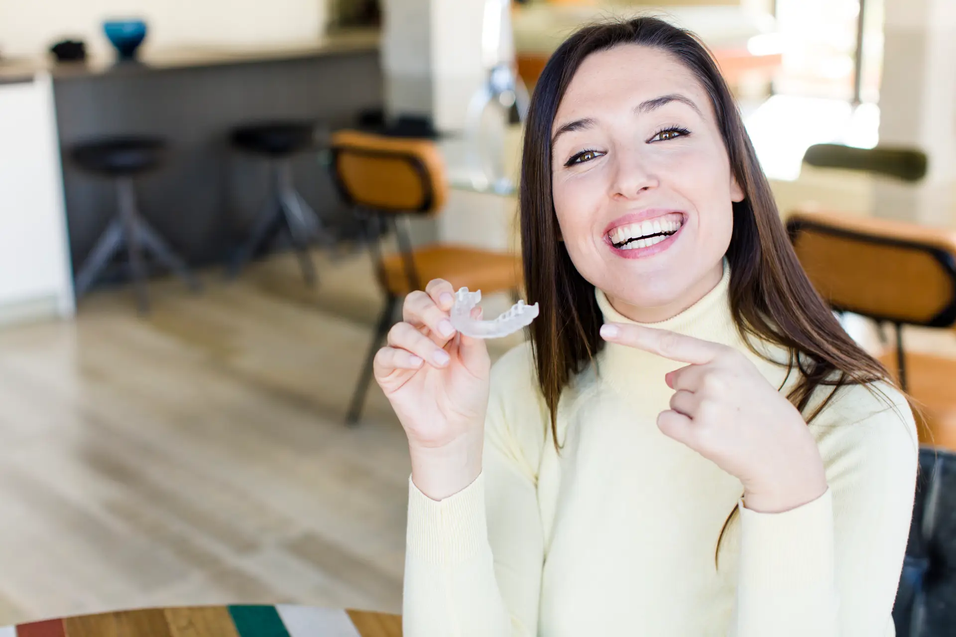 Smiling woman holding an Invisalign clear aligner at Olympic Park Smiles Dental in Calgary